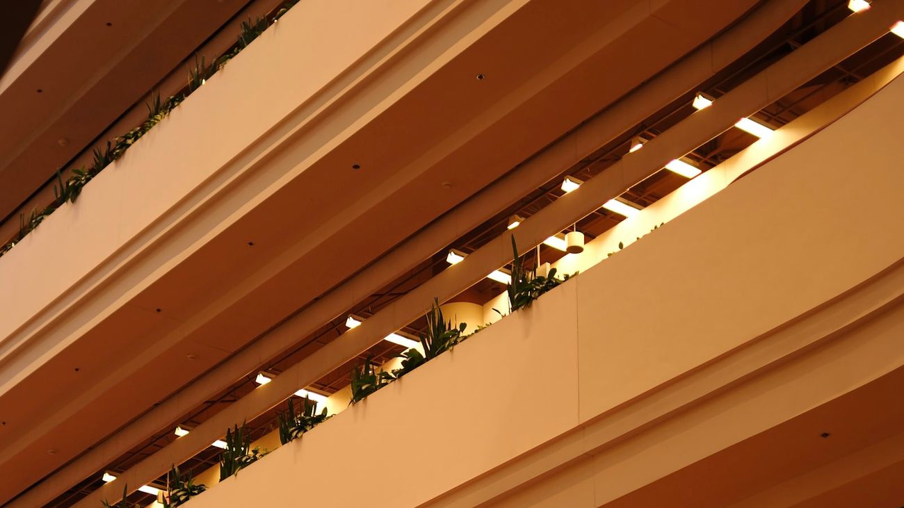 Warm cream and amber hotel balconies layered above an atrium, planting along each level