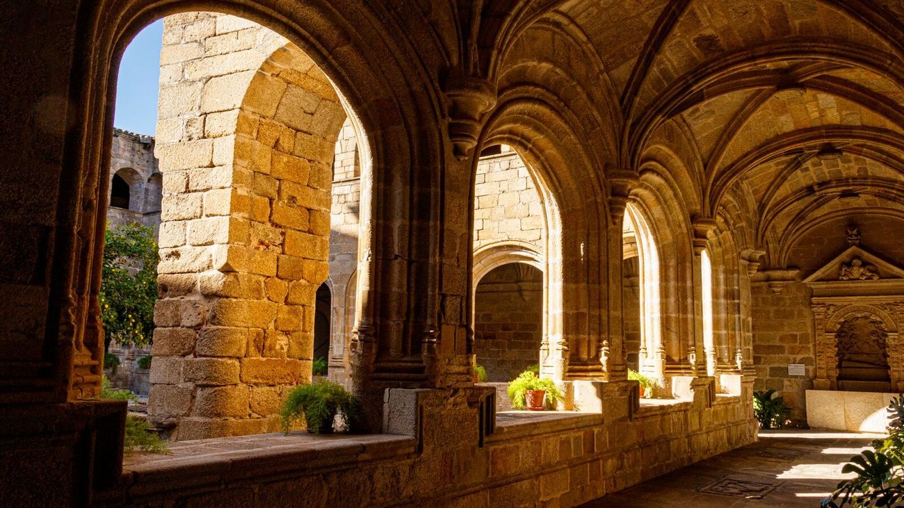 Warm sunlight falling through the stone arches of a vaulted cloister walkway.