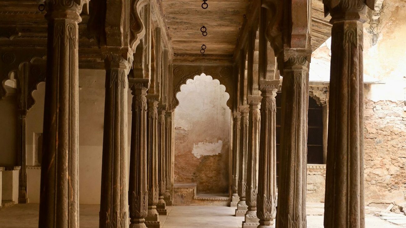 Daylight stone colonnade with carved pillars receding toward a shaped arch.