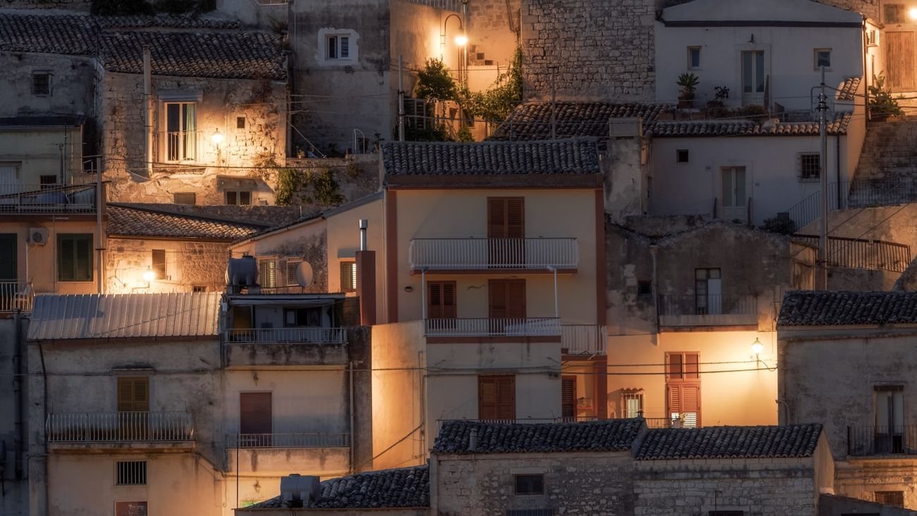 Stone hillside town at dusk, warm lamplight on shuttered facades and tiled roofs