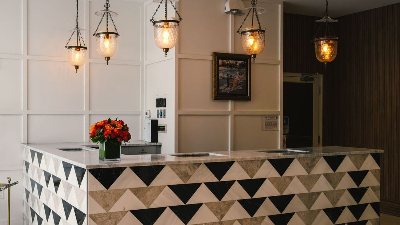 A hotel reception desk lit by warm pendant lamps, with cream panelling and a stone counter.