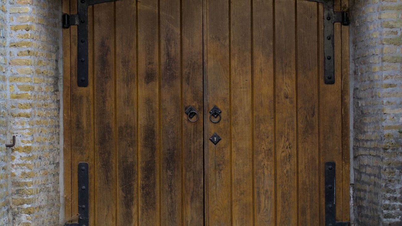 Tall double wooden doors with iron hinges inside a brick archway.