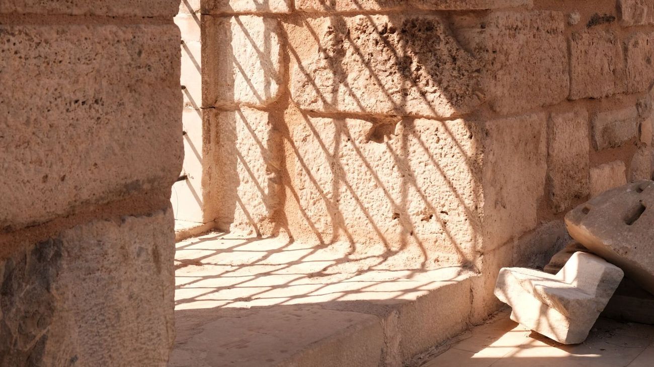 Sunlight casting a lattice of shadows across an old sandstone wall and ledge.