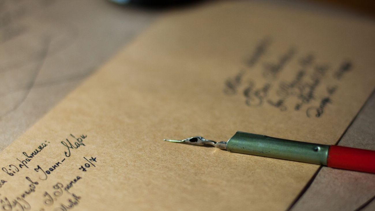 A handwritten kraft envelope and a dip pen resting on a wooden desk.