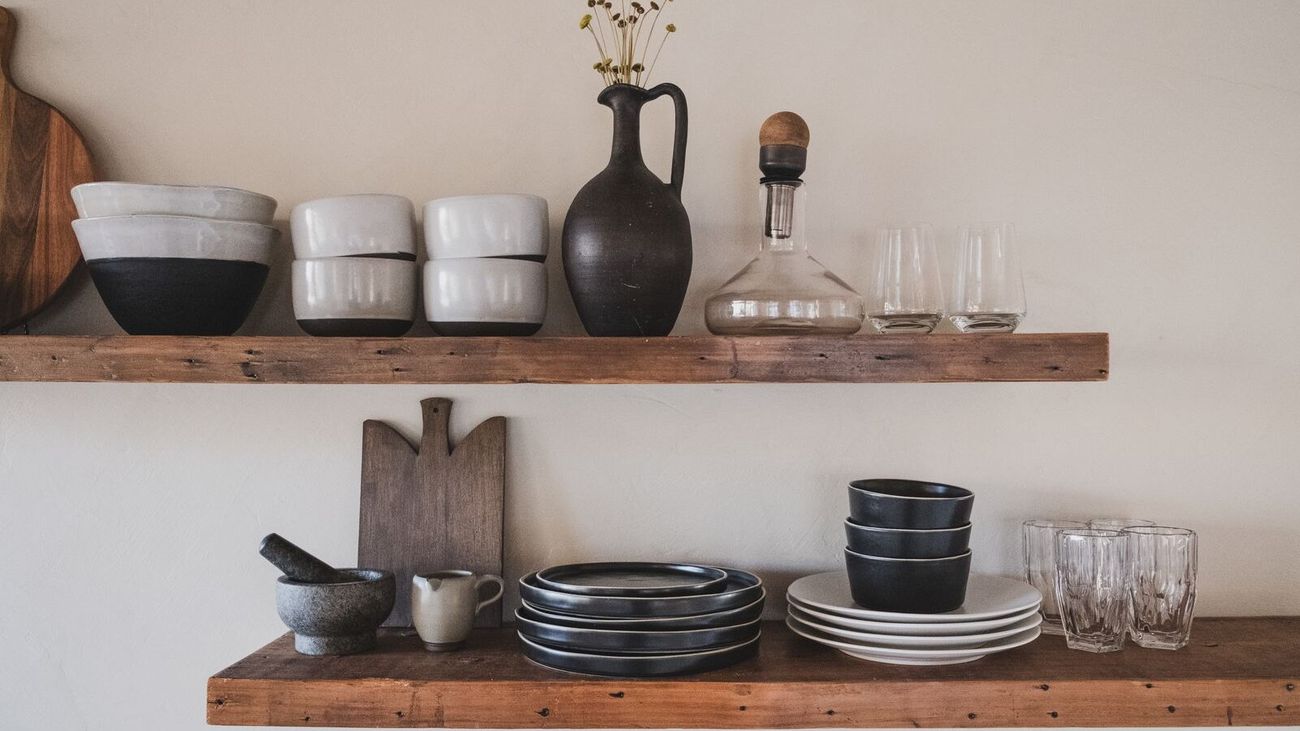 Stacked ceramic bowls, plates and glassware on rustic wooden shelves.