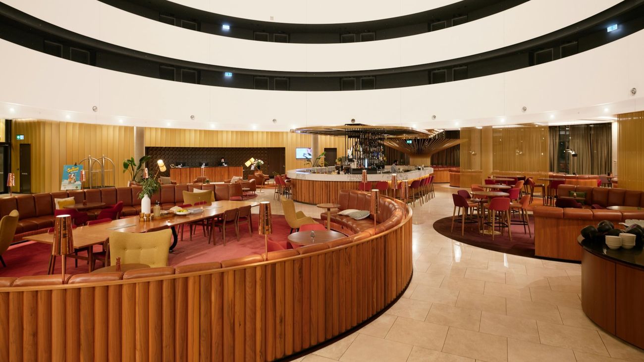 A curved wooden banquette winding through a warm hotel lobby lounge with a round bar