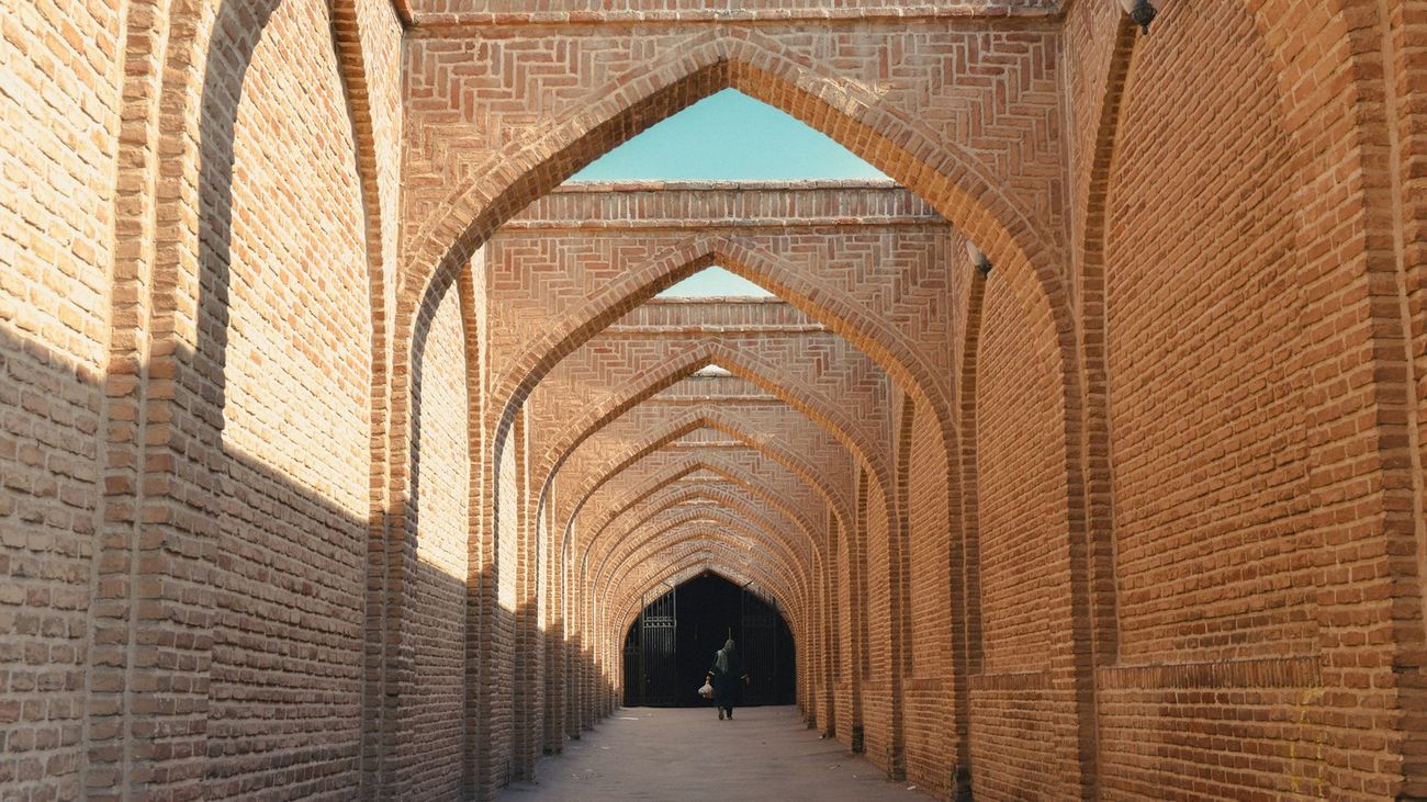 A long brick arcade of repeating pointed arches in warm afternoon light