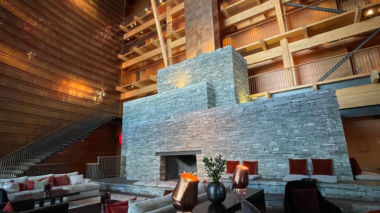 A hotel lobby in warm wood and stacked stone, with a double-height fireplace and lit candles on the low tables.