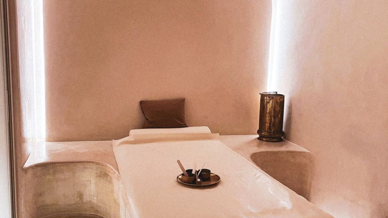 A quiet massage room with cream plaster walls and a made-up treatment bed.