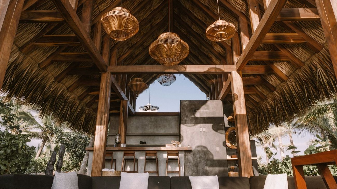 A wooden palapa pavilion with woven pendant lamps hanging under a thatched roof.