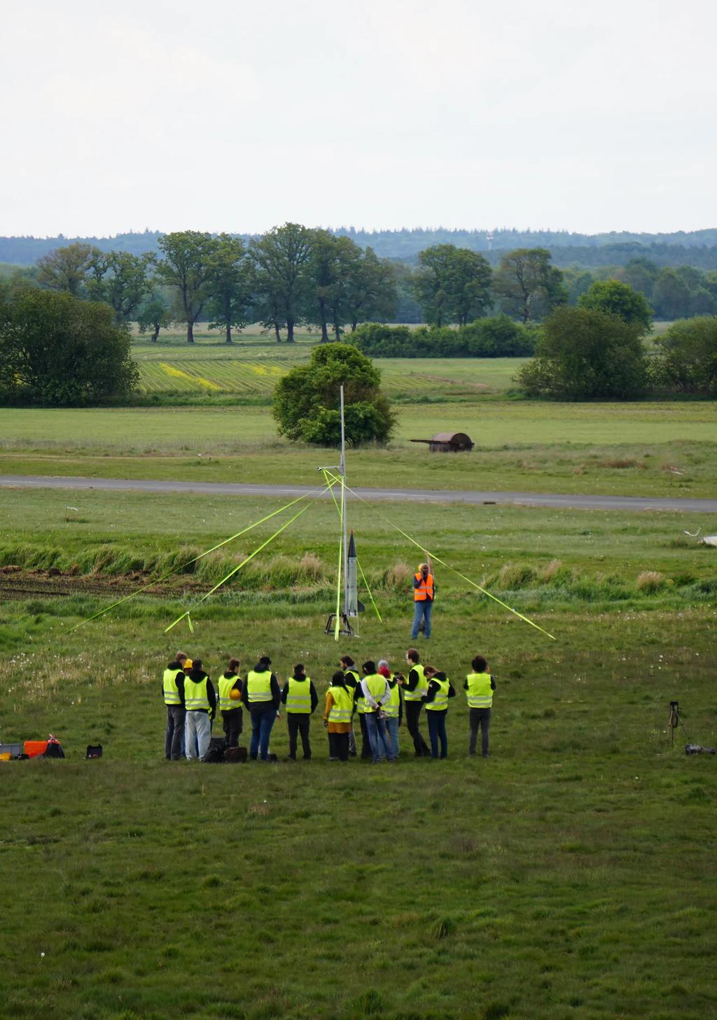 Group of students crowded around a launch rail in a field holding the Ascendance rocket