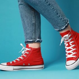các hãng giày nổi tiếng đôi chân phụ nữ mặc quần jean dài mang giày converse màu đỏ trên nền xanh ngọc