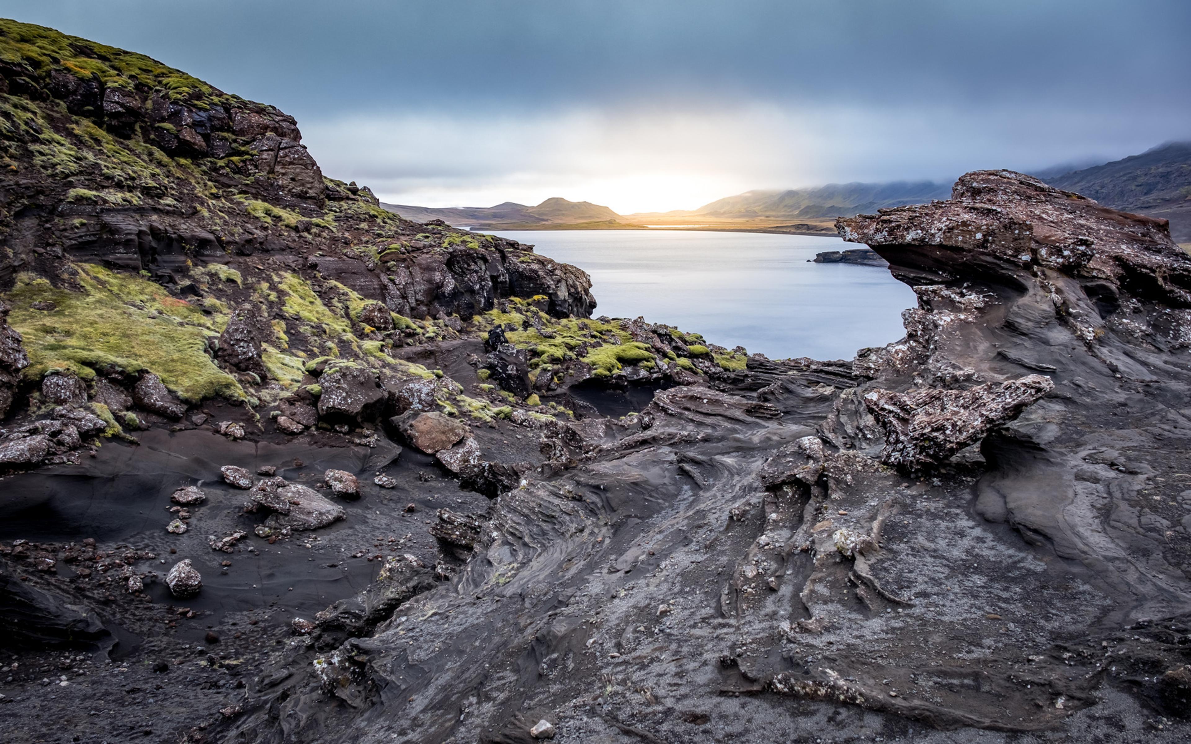 Campos de lava cubiertos de musgo junto al mar con el sol muy bajo en el horizonte, Islandia