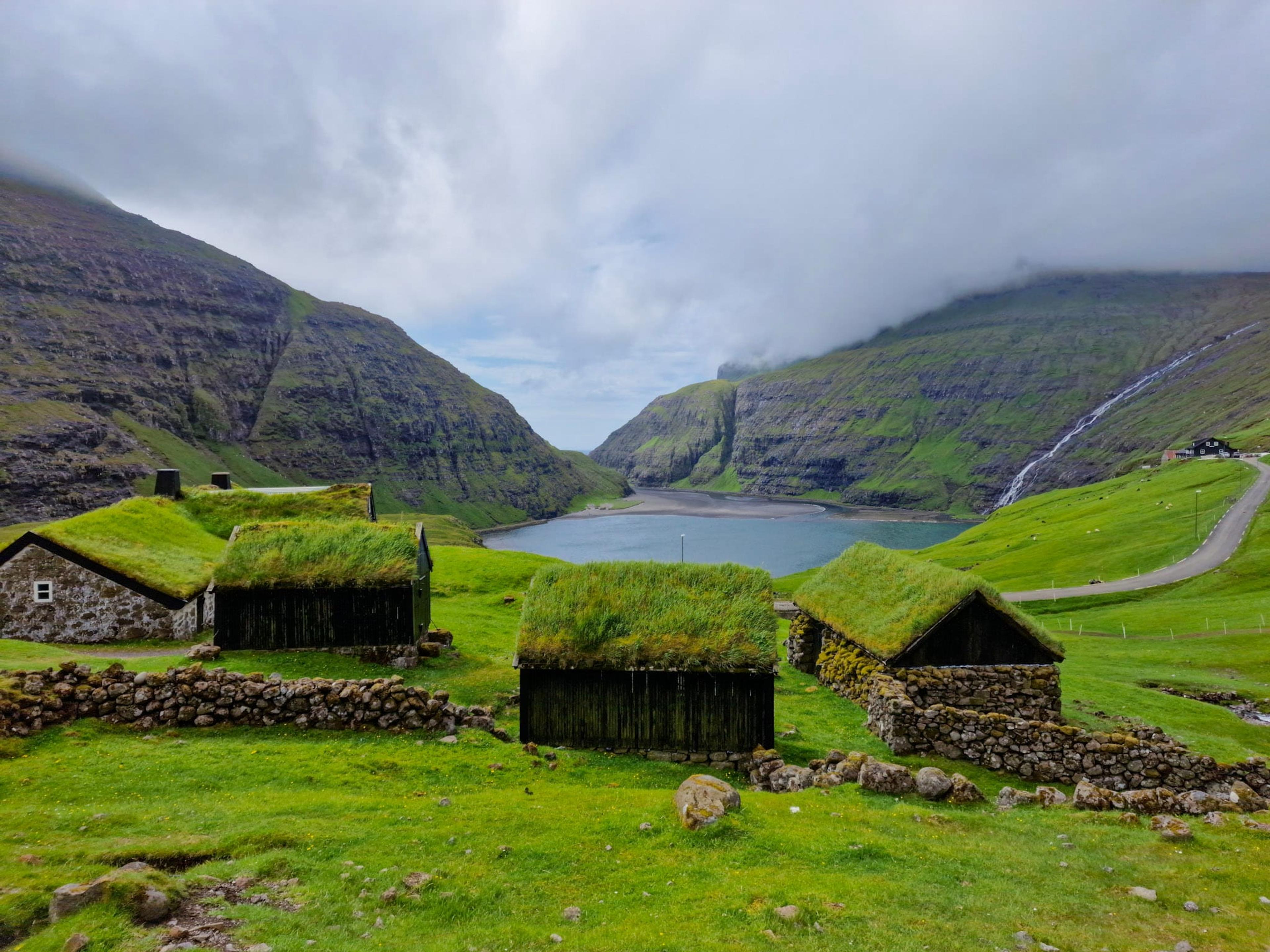 Casas de cubierta de hierba frente a la laguna de Saksun rodeada de montañas verdes, isla de Streymoy
