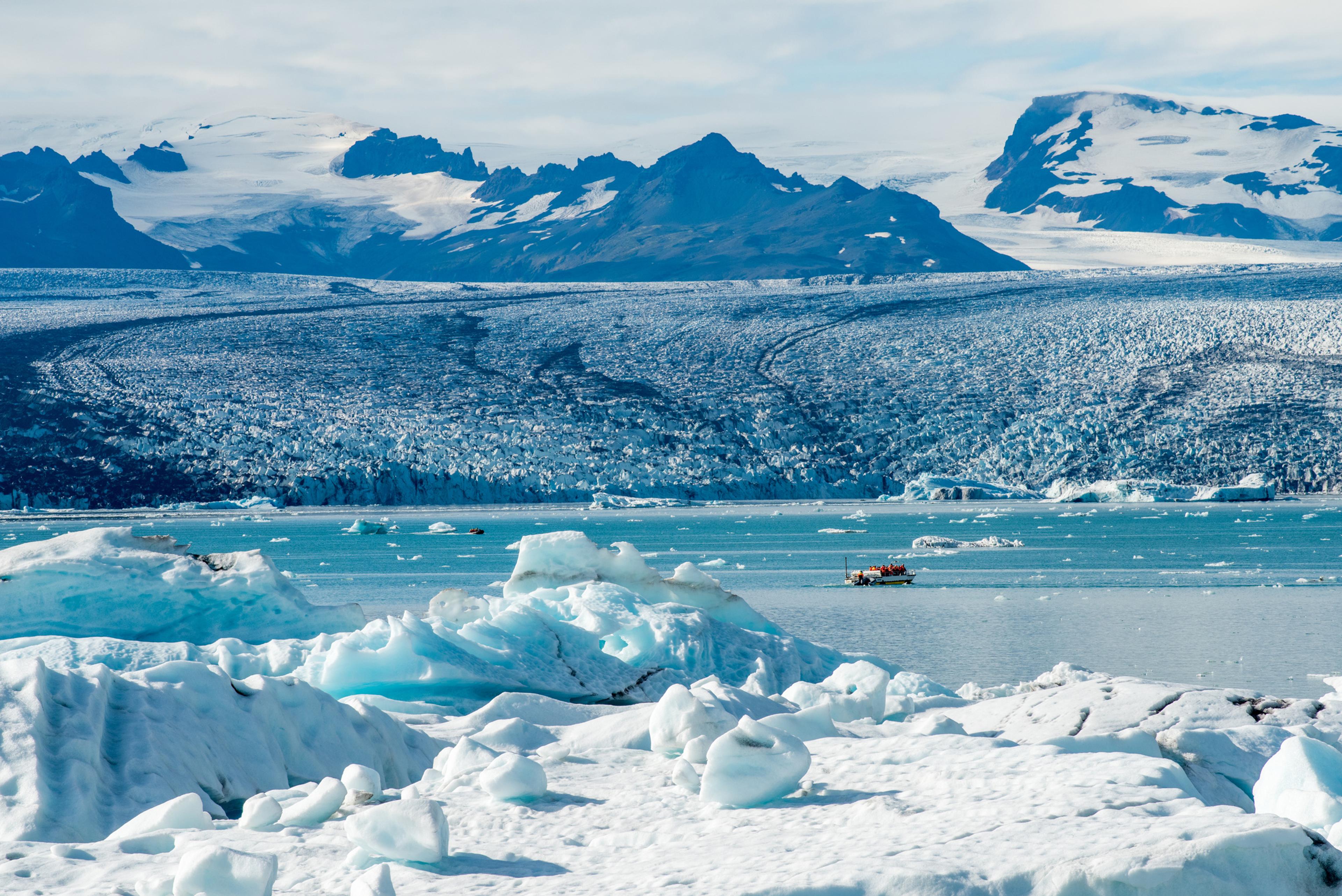 Lengua del glaciar Vatnajökull descendiendo hacia la laguna, con icebergs y una barca navegando entre ellos