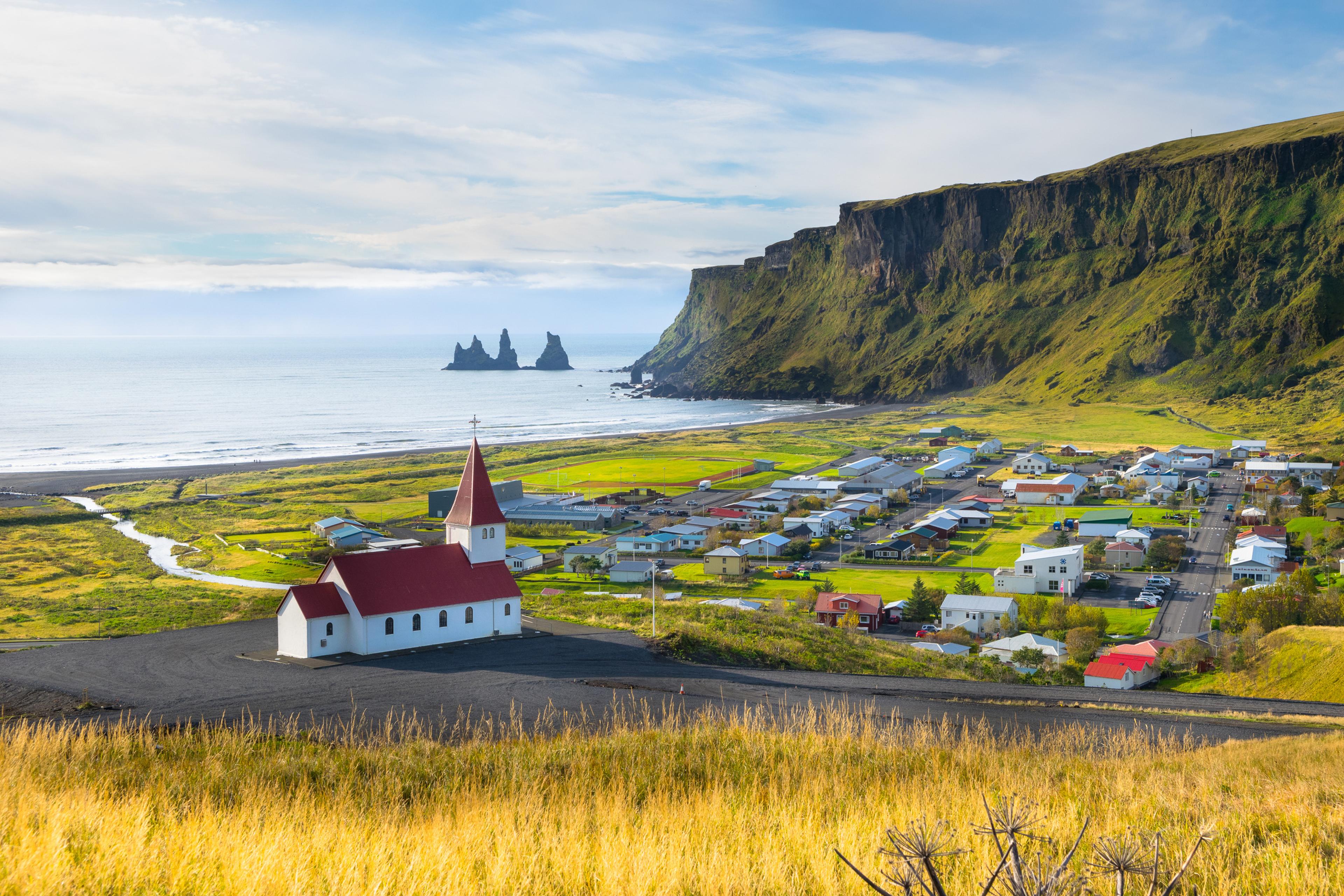 La iglesia de Vík sobre la ladera verde con el mar y los farallones de Reynisdrangar al fondo
