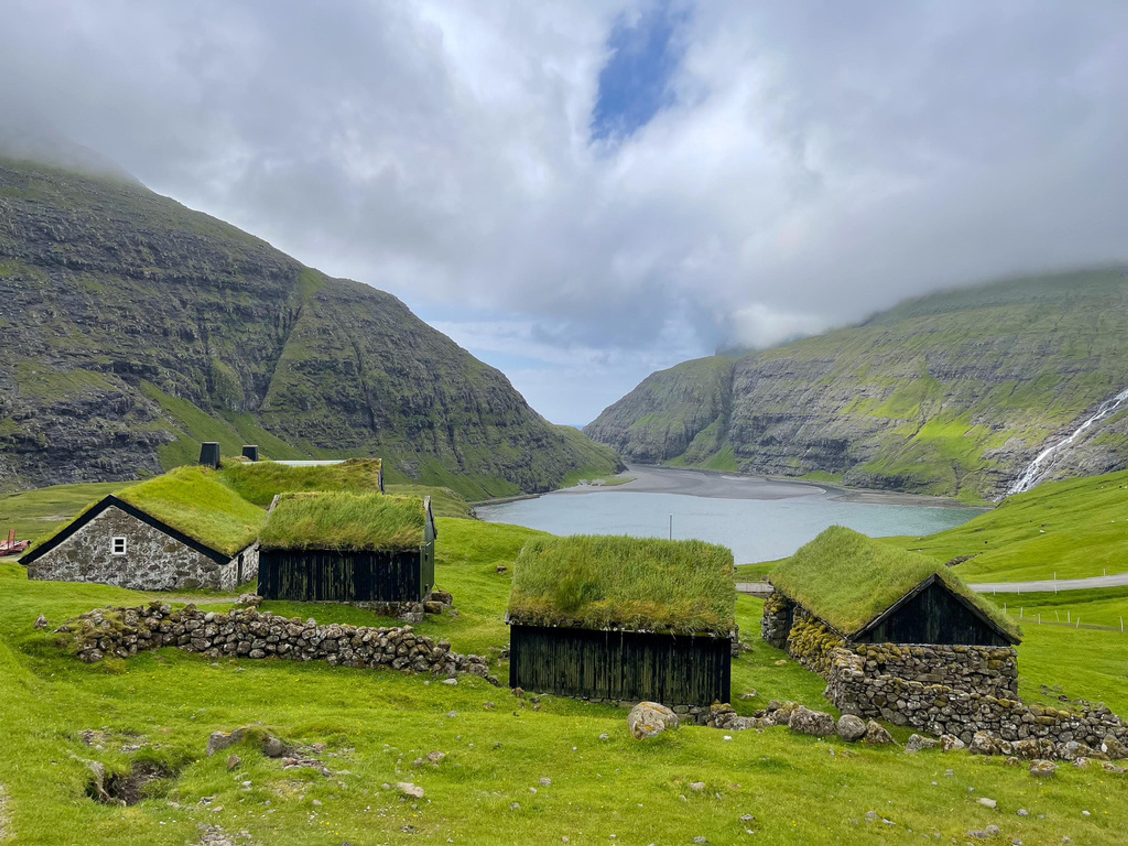Casas de piedra con cubierta de hierba junto a una laguna rodeada de montañas en las Islas Feroe