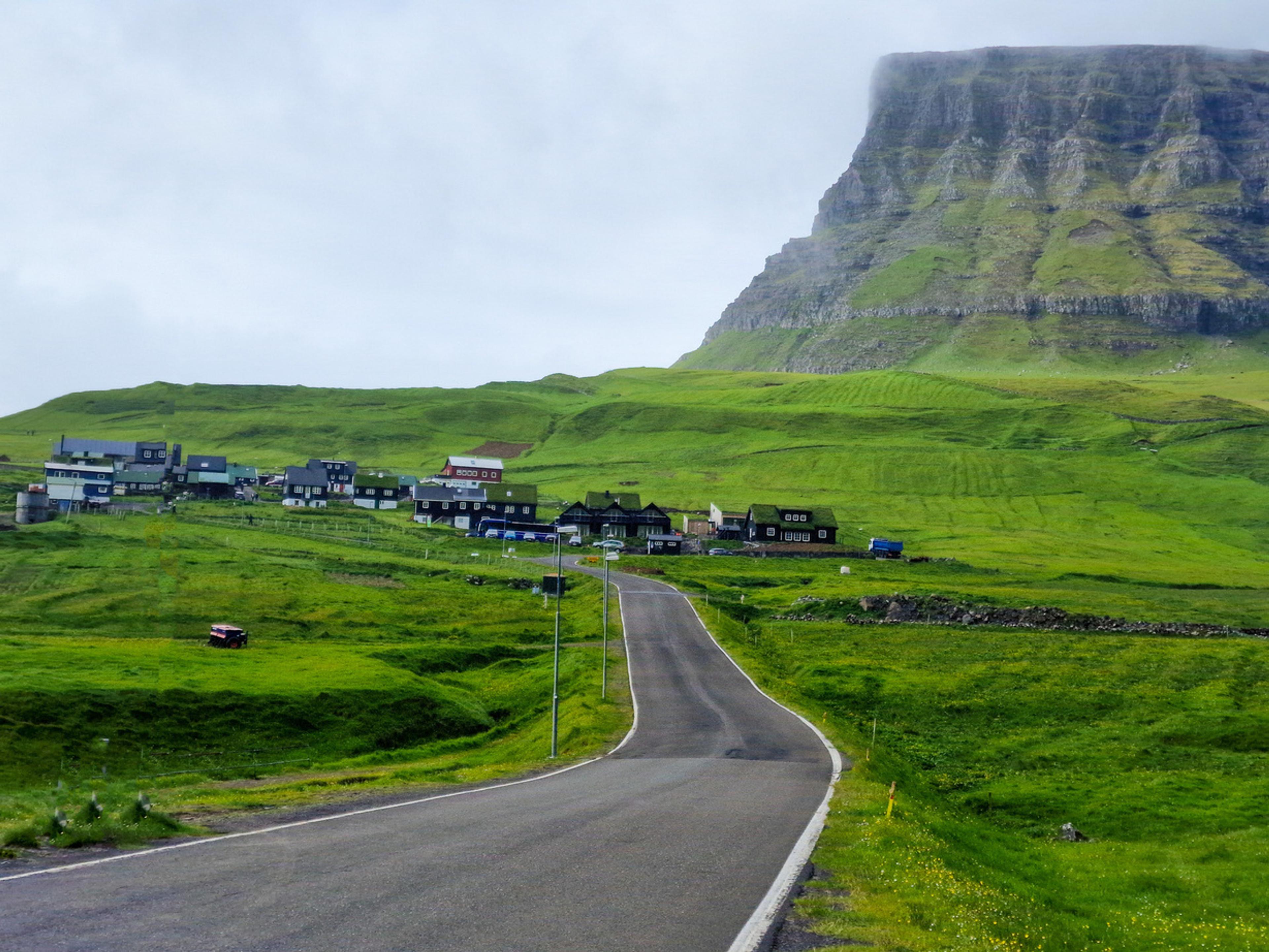 Carretera llegando al pueblo de Gásadalur bajo una montaña de cima plana, isla de Vágar