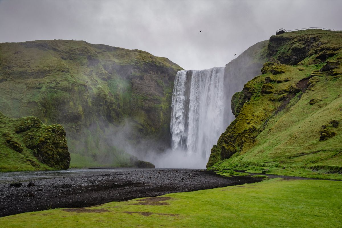 La cascada Skógafoss cayendo entre laderas verdes en verano, costa sur de Islandia
