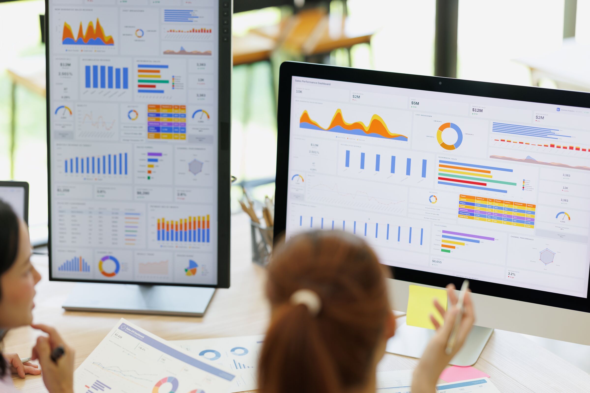 Colleagues reviewing analytics dashboards on two screens