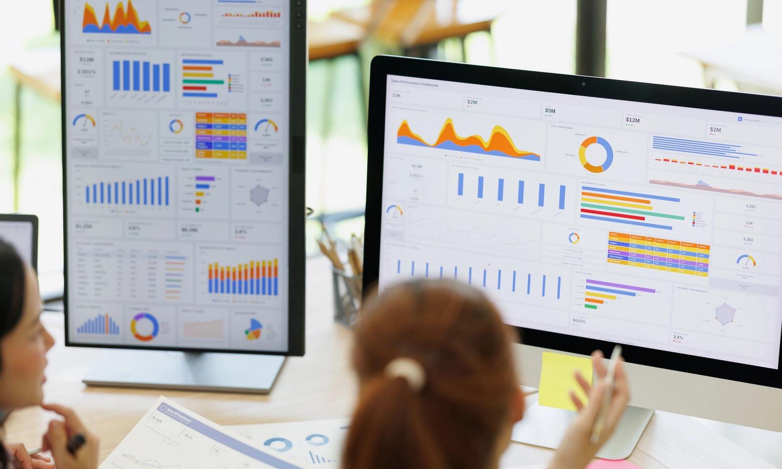 Colleagues reviewing analytics dashboards on two screens