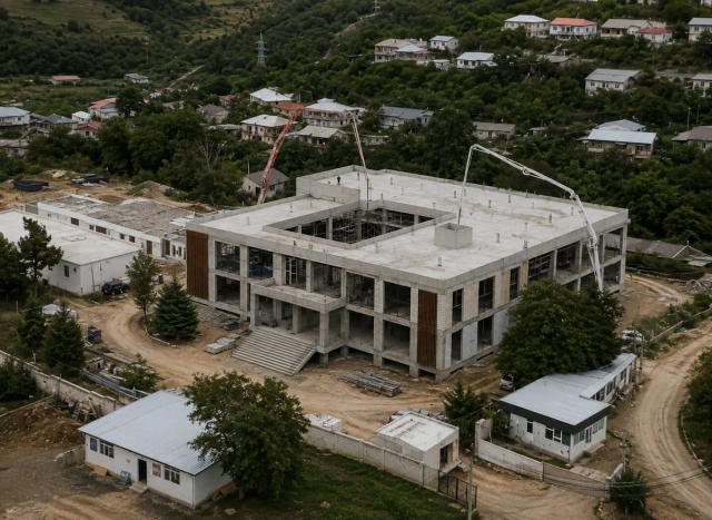 Concrete being placed on the top slab of a building at a substation project using two concrete pumps — an aerial view with residential houses around