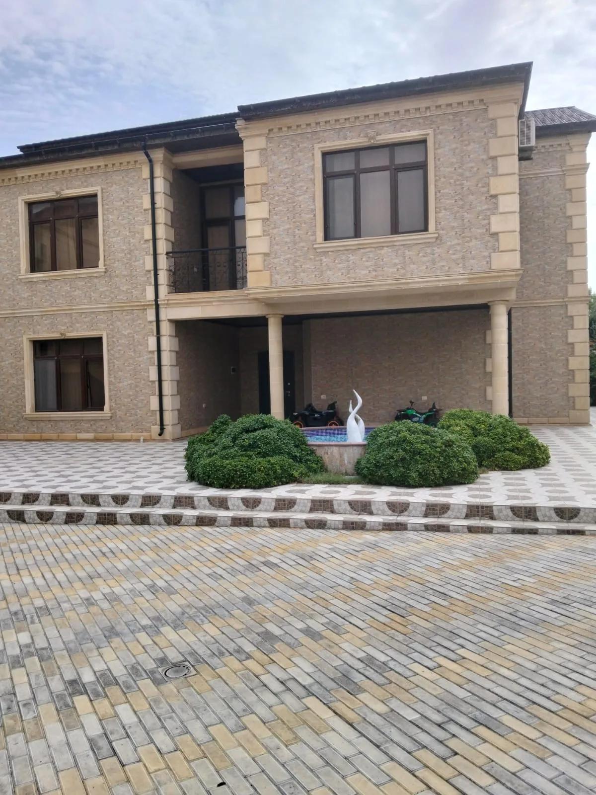 İkimərtəbəli fərdi yaşayış evi — daş üzlüklü fasad, sütunlu eyvan və döşəmə örtüklü həyət