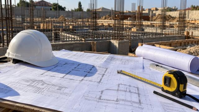 Tikinti meydançasında masa üzərində işçi çertyojları və kaska