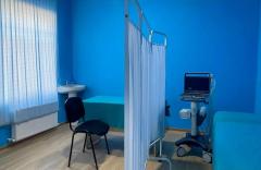 Examination room — blue walls, a curtain partition, an examination couch, an ultrasound unit and a new radiator