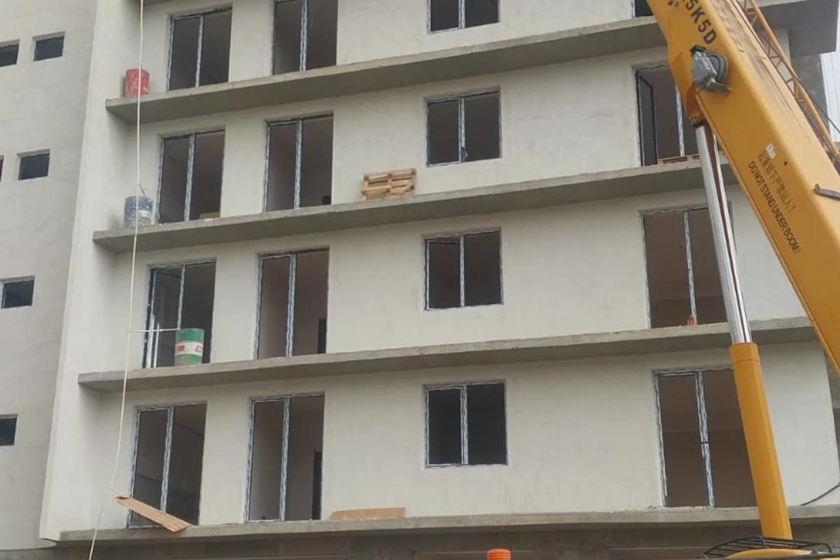 Facade work on a five-storey residential building — a mobile crane lifting materials, shopfront openings still open on the lower floors
