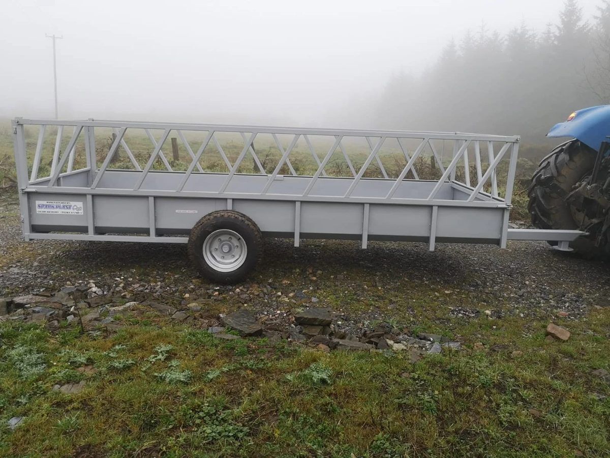 Grey silage feeding trailer with diagonal feed barriers, hitched to a tractor