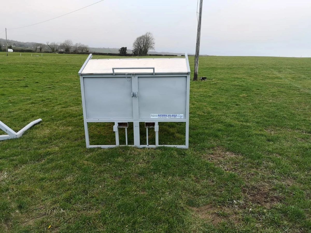 Galvanised calf creep feeder with a hinged lid, standing in a field
