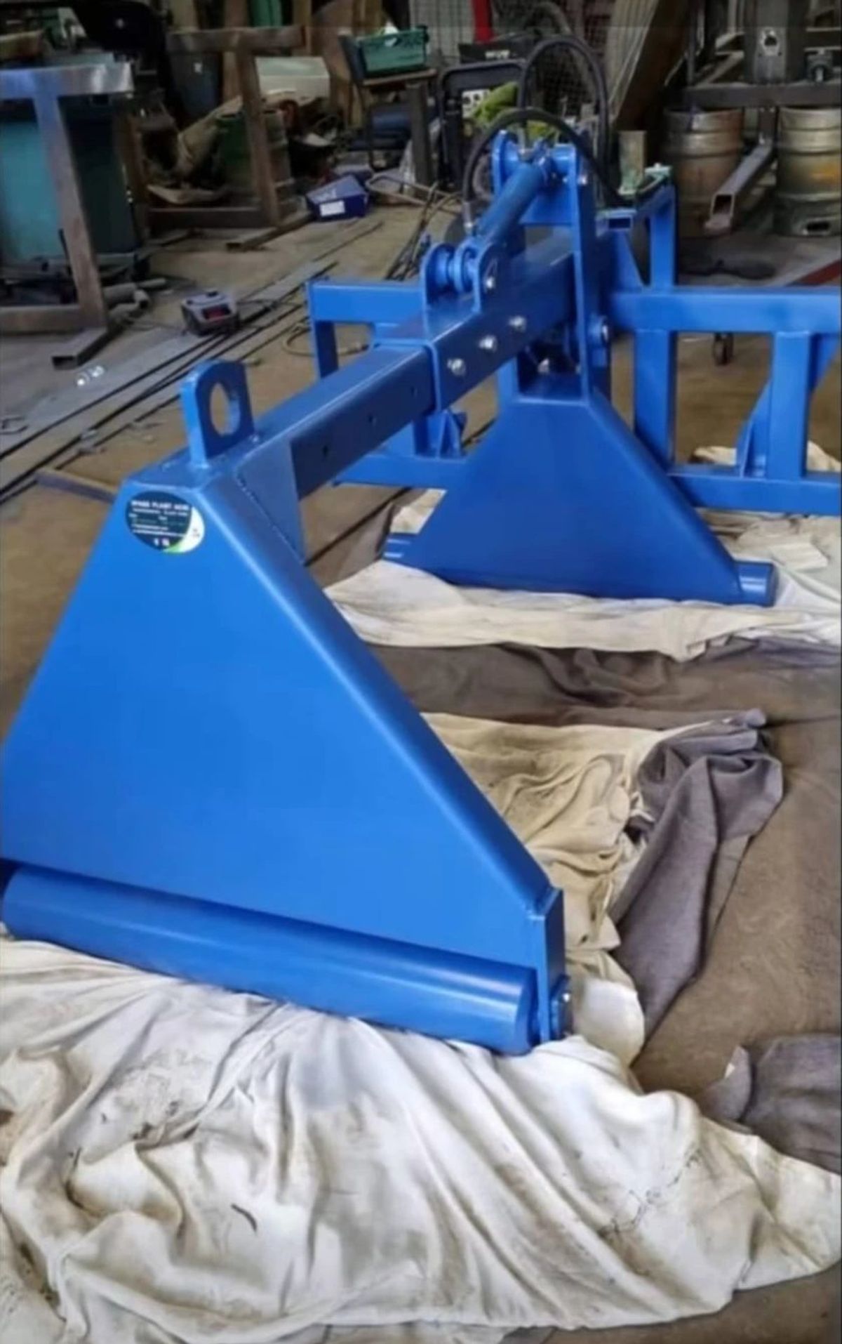 Blue soft squeeze bale handler with two squeeze arms and a hydraulic ram, in the workshop