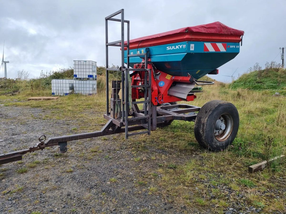 Fertiliser bogie in bare steel with a drawbar, jockey wheel and ladder, carrying a fertiliser spreader