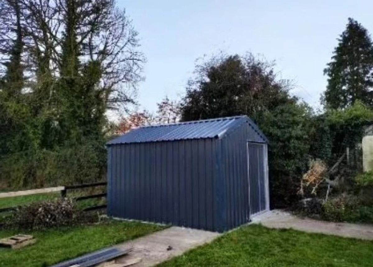 Finished grey steel garden shed with a sliding door, in a garden
