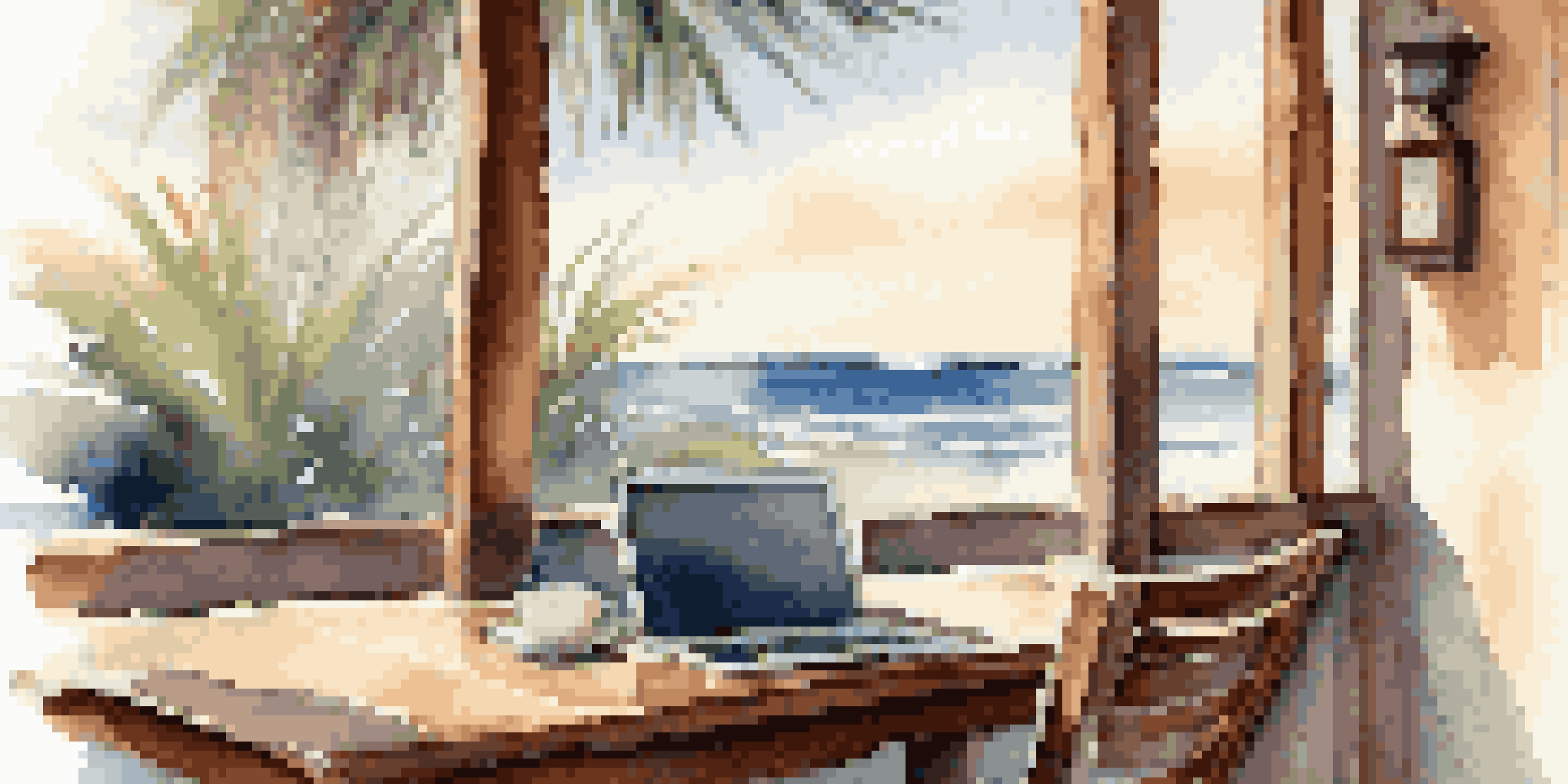 A beachside café with a laptop on a table, palm trees, and the ocean in the background under warm morning light.