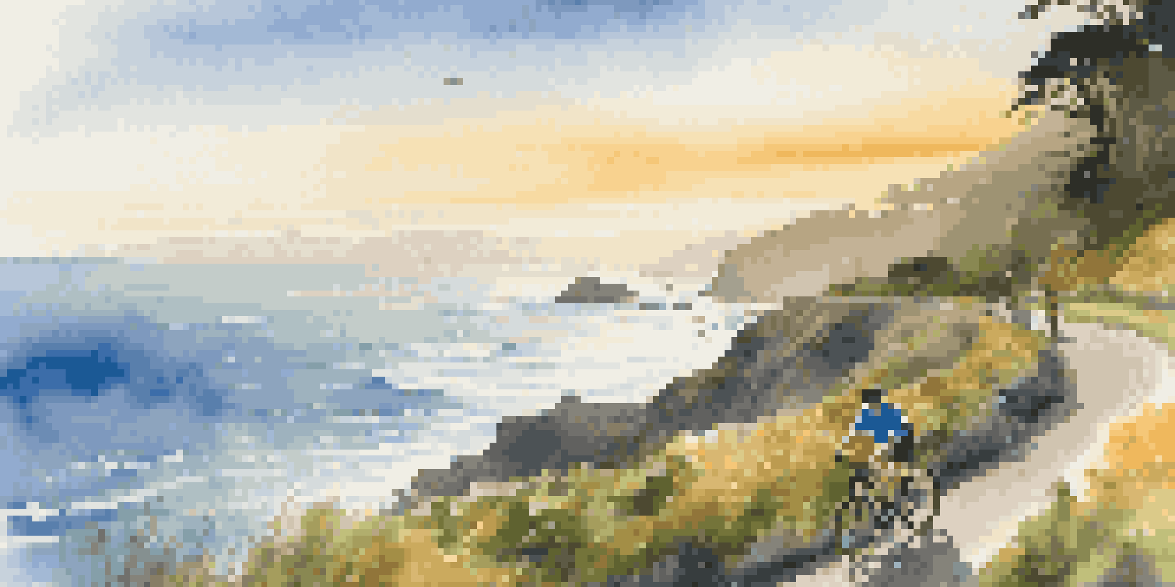 A cyclist riding along the Pacific Coast Highway during sunset, with ocean waves crashing against the cliffs below.