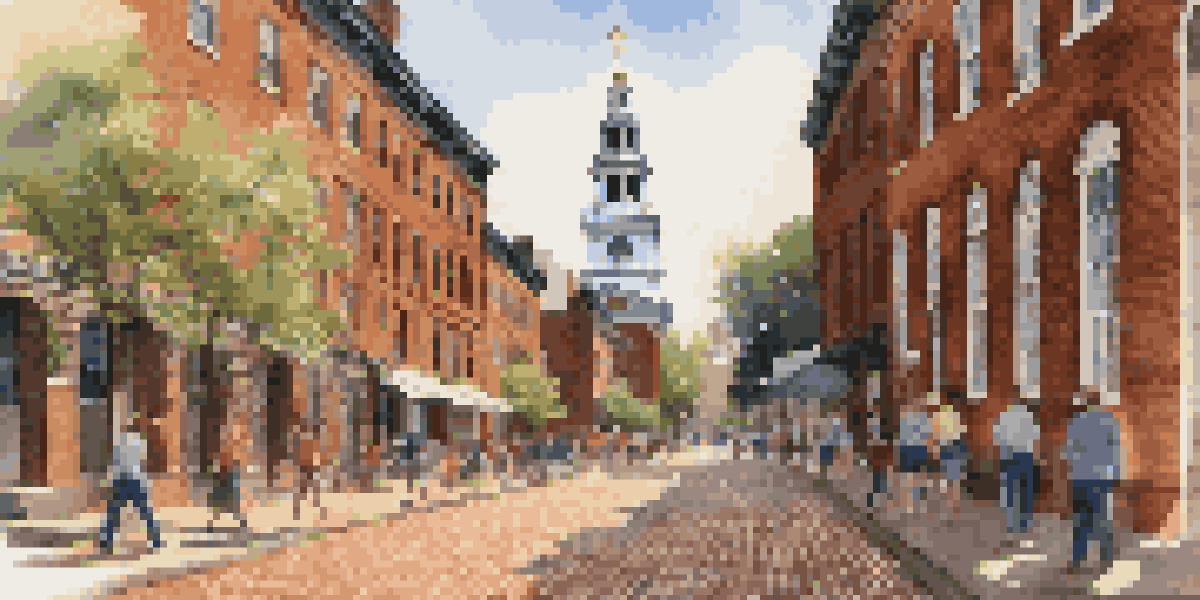 A cobblestone street in Philadelphia with historic buildings and Independence Hall in the background, illuminated by warm sunlight.