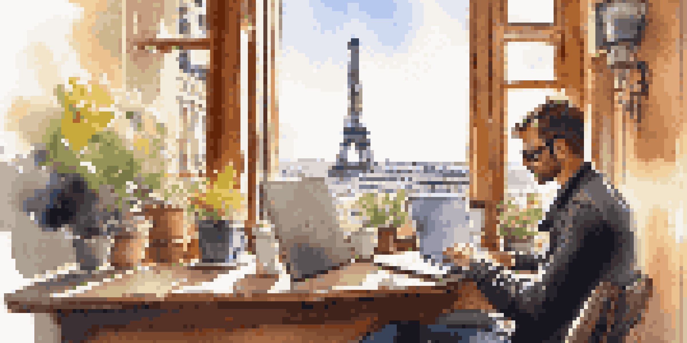 A person working on a laptop in a Paris café, with coffee and the Eiffel Tower visible outside.