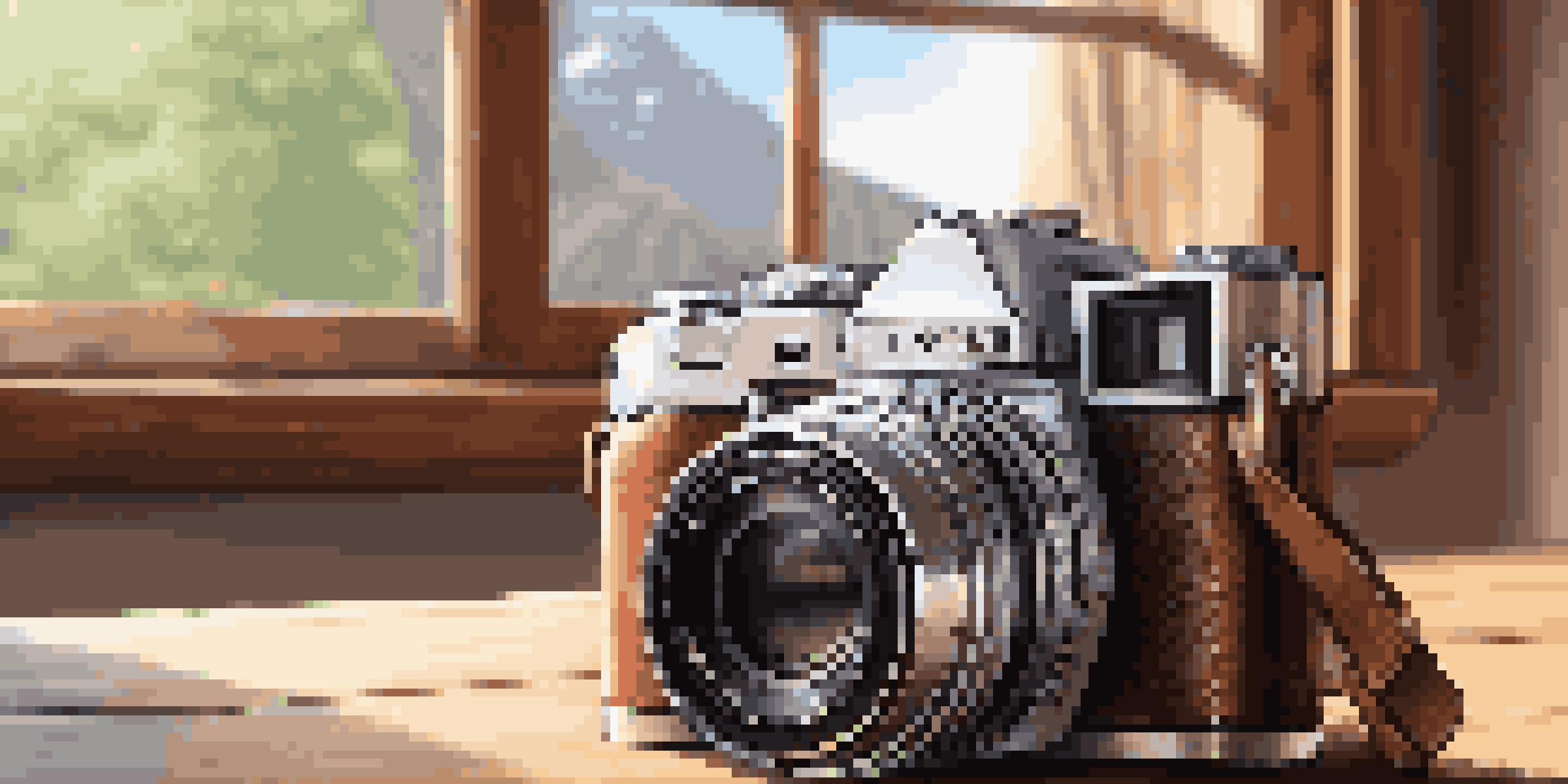 A compact mirrorless camera on a wooden table with a lightweight camera bag and a prime lens, illuminated by soft natural light.