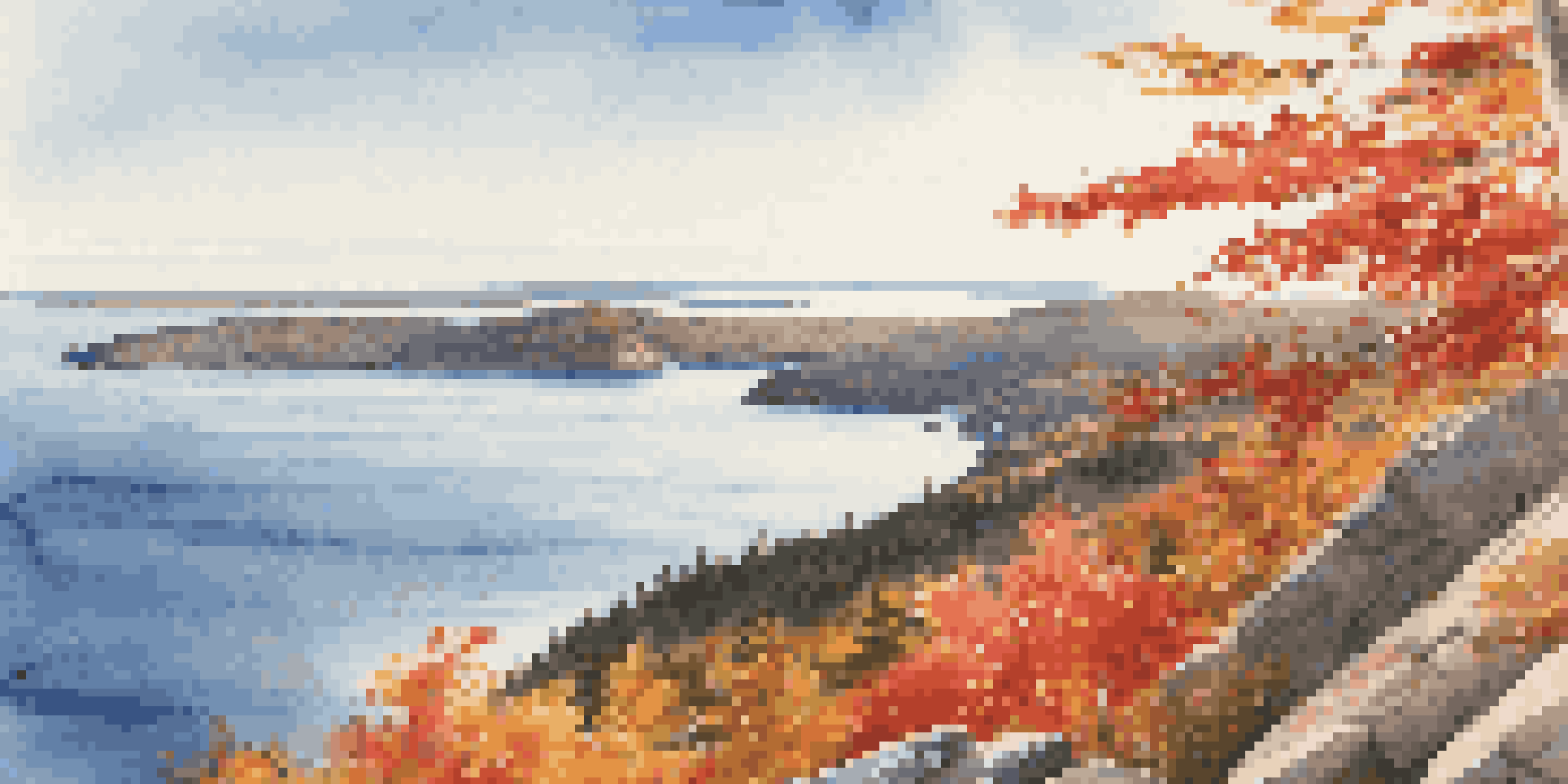 A scenic view of Acadia National Park in Maine, featuring autumn foliage in vibrant red and orange colors alongside a blue ocean, viewed from Cadillac Mountain under warm sunlight.