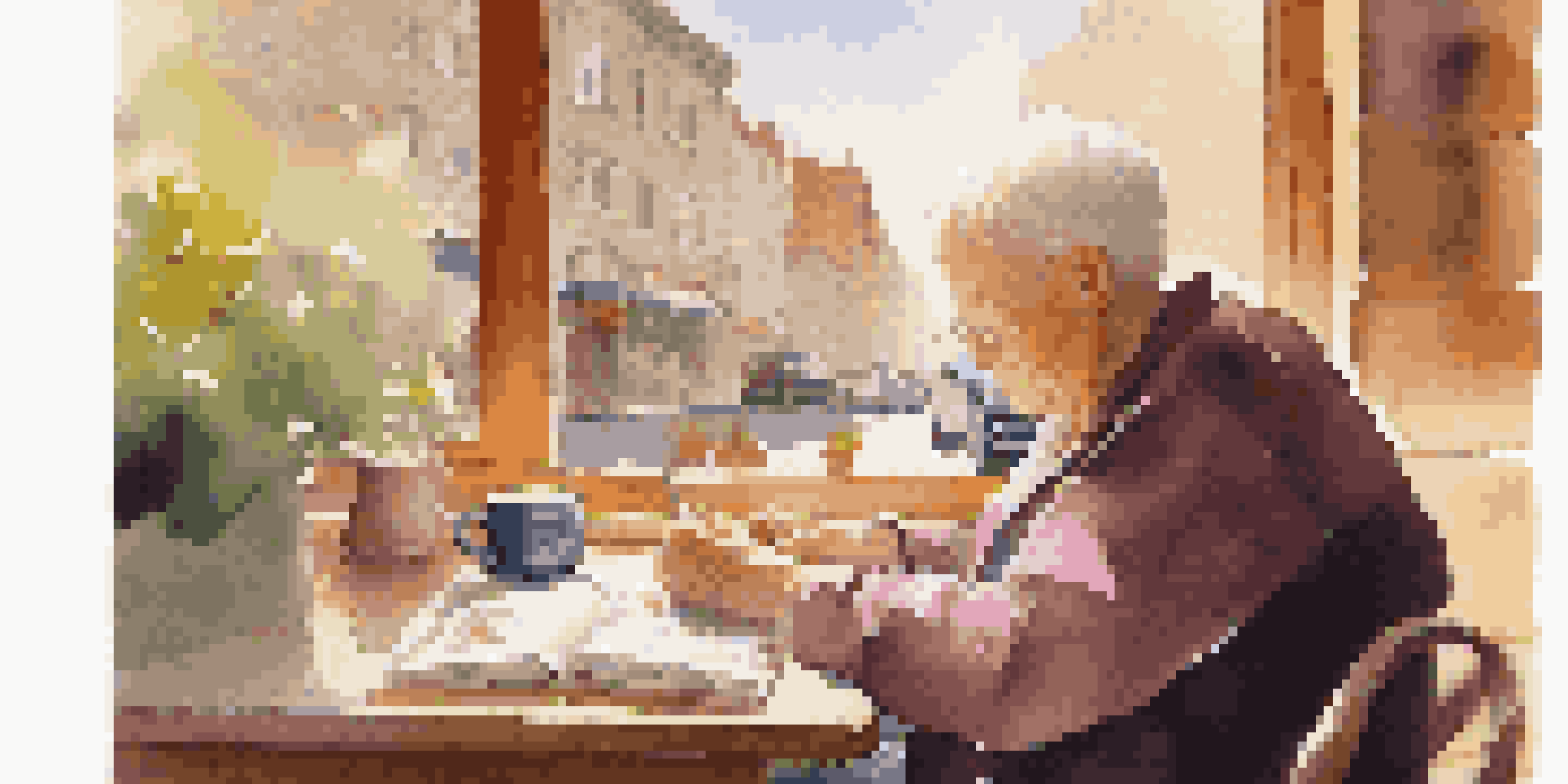 An elderly person writing in a travel journal at a café, with a cup of coffee and travel mementos on the table.