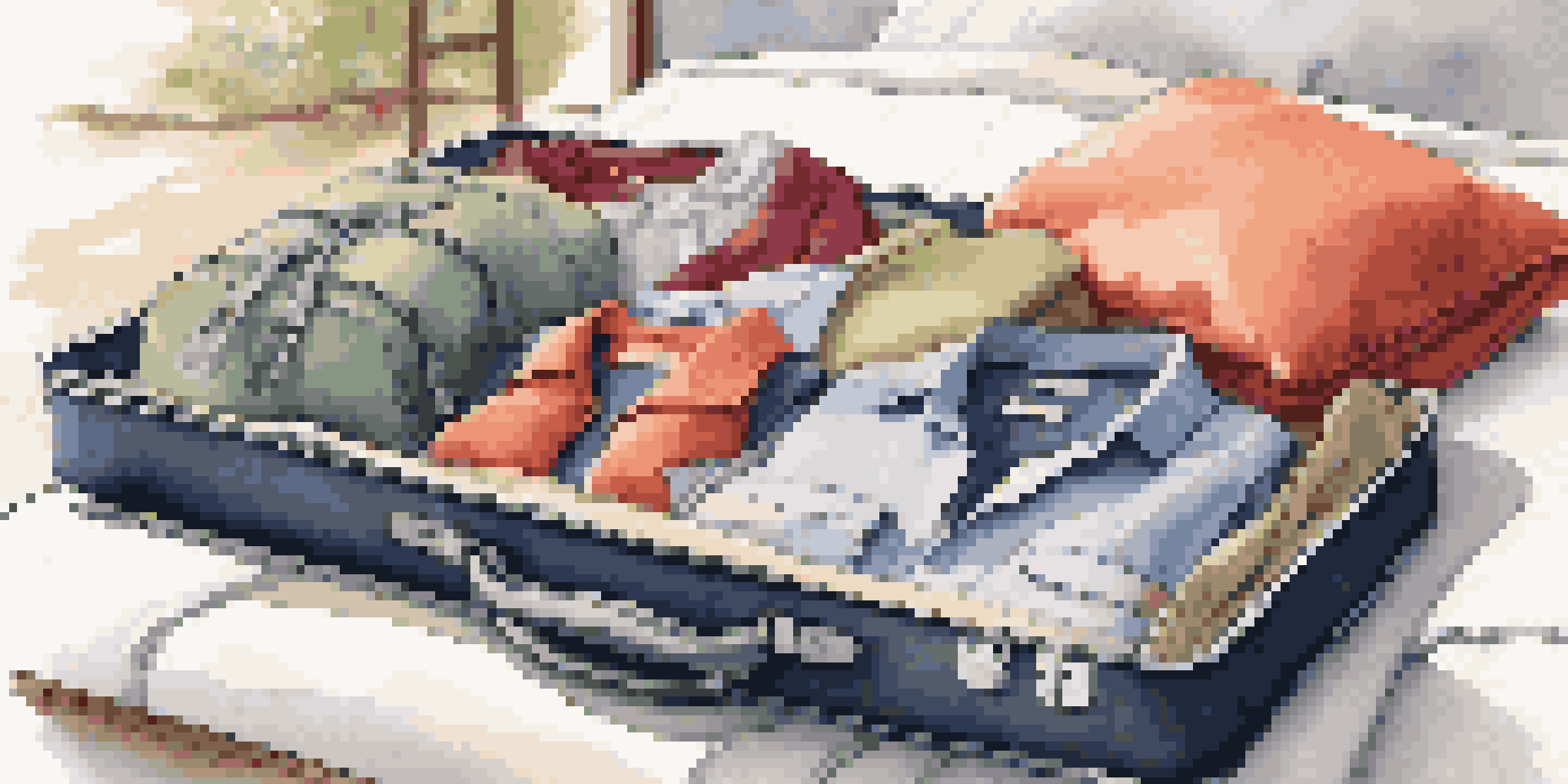 An open carry-on suitcase on a bed filled with colorful packing cubes and clothing, illuminated by natural sunlight.