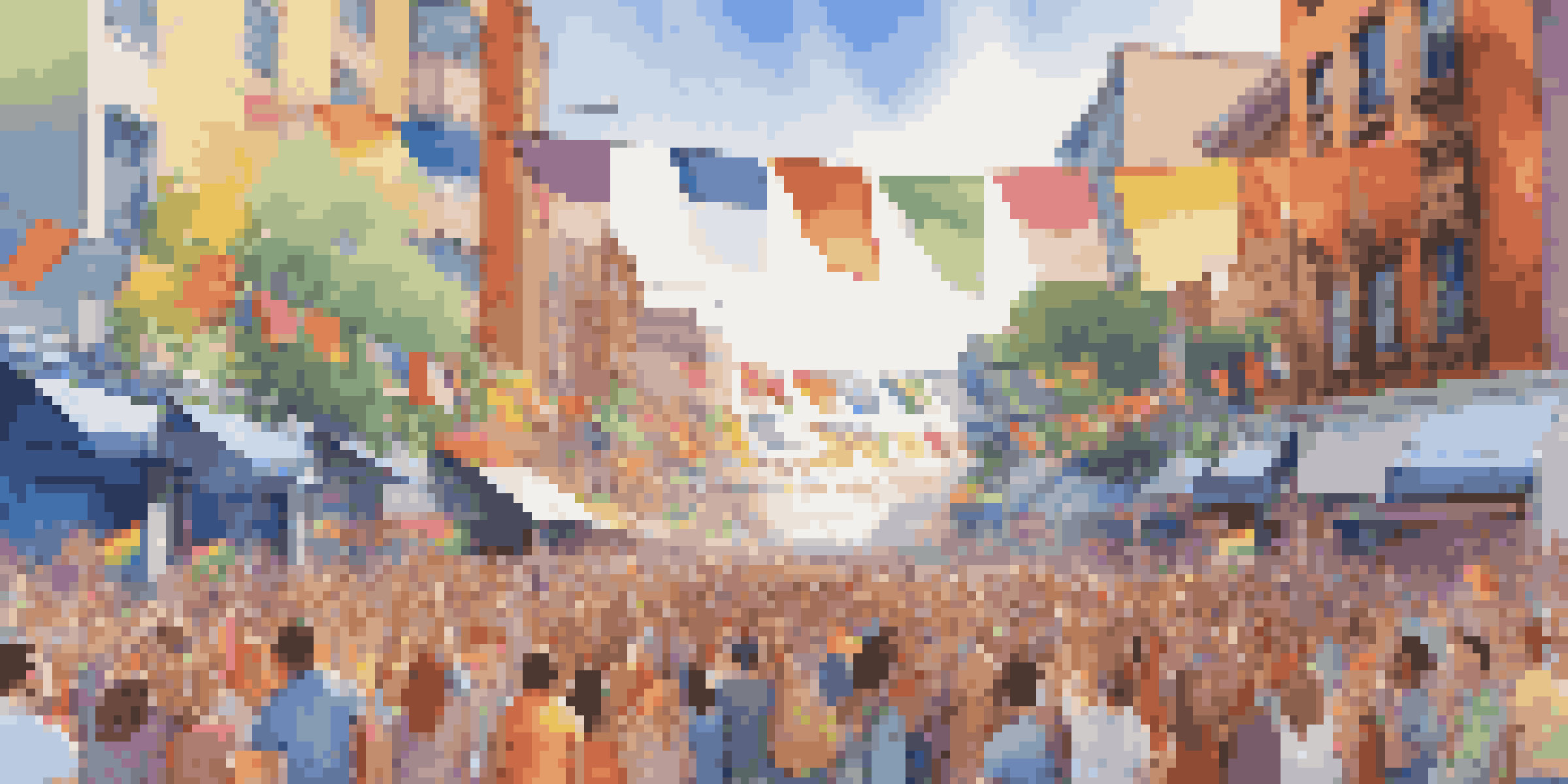 A lively LGBTQ+ pride parade in an urban area with colorful flags and diverse people celebrating under a clear blue sky.