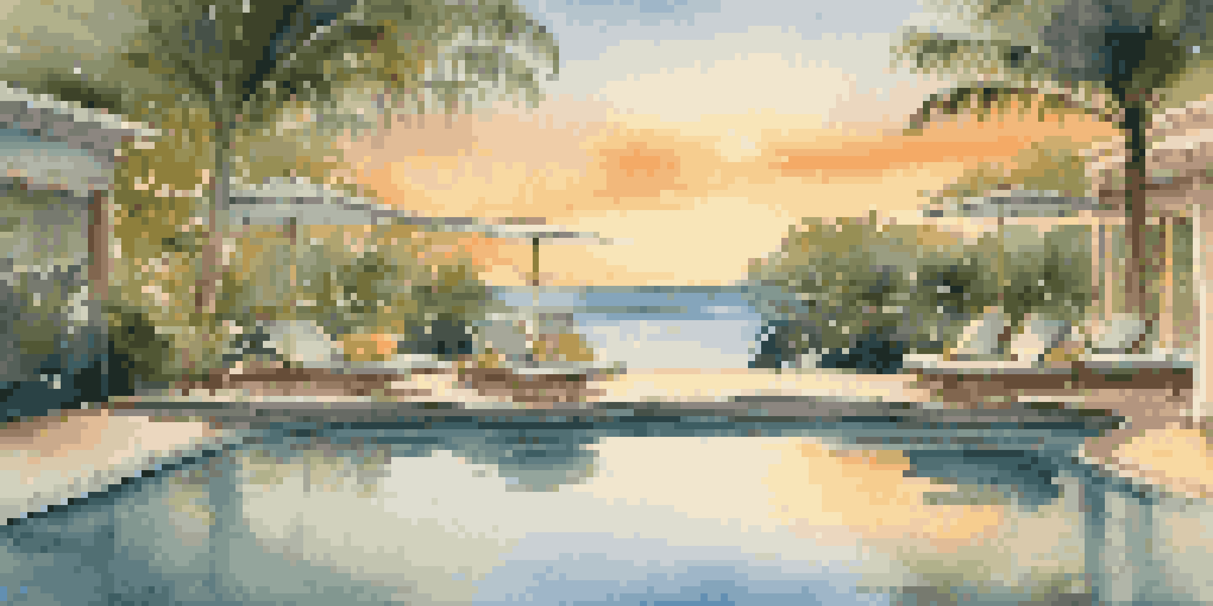 A peaceful luxury hotel pool at sunset with cocktails on a table, surrounded by tropical plants.