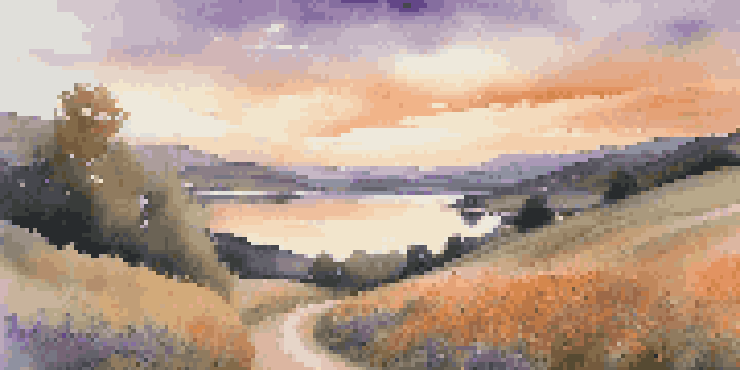 A beautiful landscape during sunset, featuring hills, a winding path with wildflowers, and a calm lake reflecting the colorful sky.