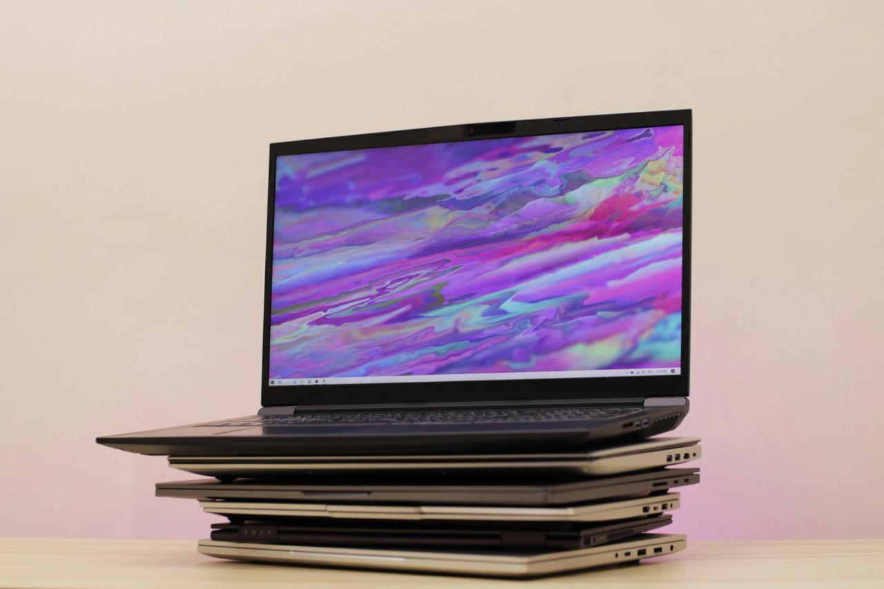 A gaming laptop open on top of a stack of closed laptops.