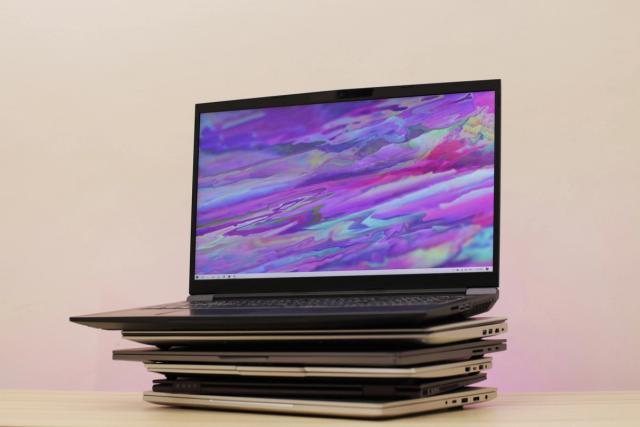 A gaming laptop open on top of a stack of closed laptops.