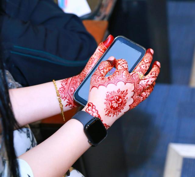 Hands decorated with henna holding a smartphone, photographed in Karachi.