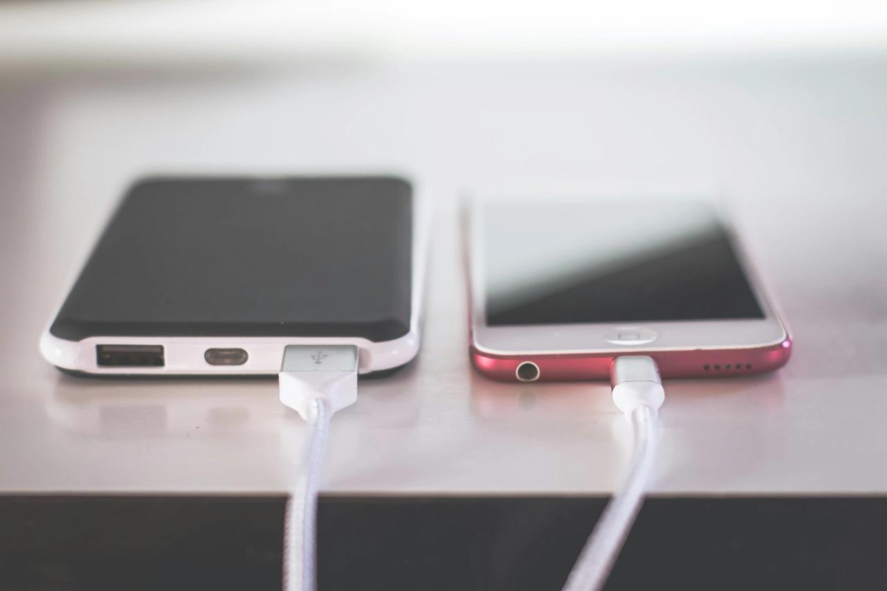 A power bank and a phone side by side on a table, both plugged in with charging cables.